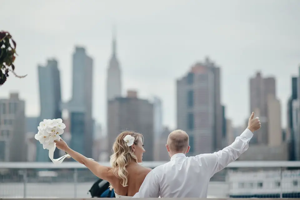 Seen from behind, the bride and groom raise their arms to the Midtown skyline and the Empire State Building.