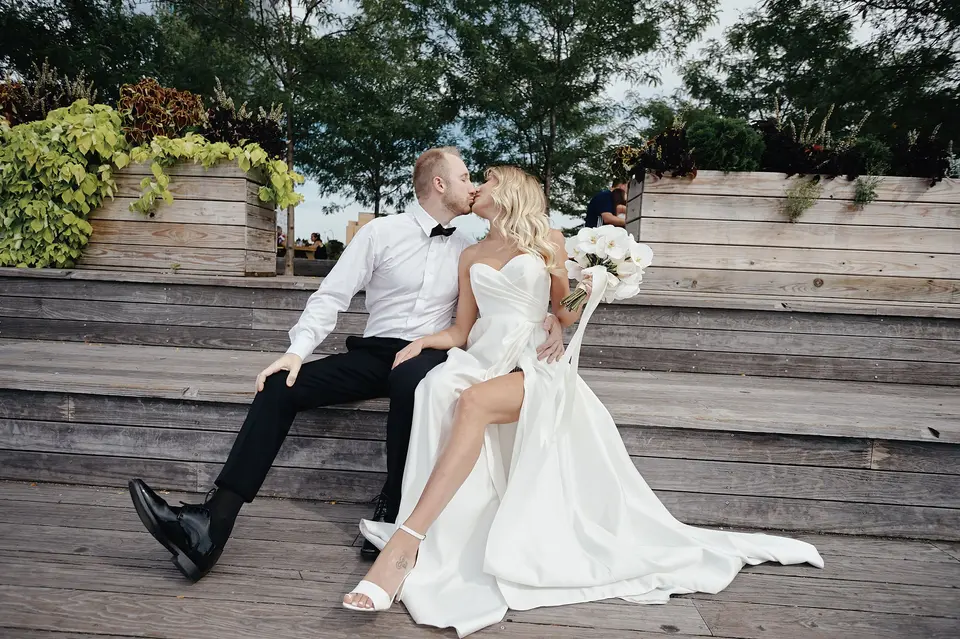 The couple kiss on the wooden steps of a waterfront park.