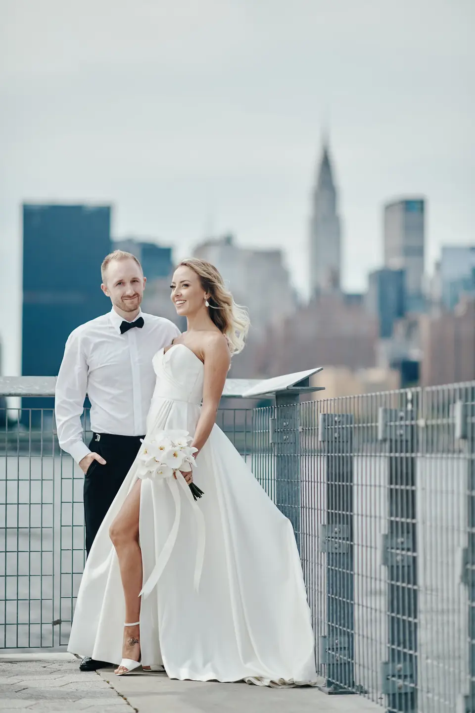 The bride and groom by the railing on the waterfront, the Chrysler Building across the river.