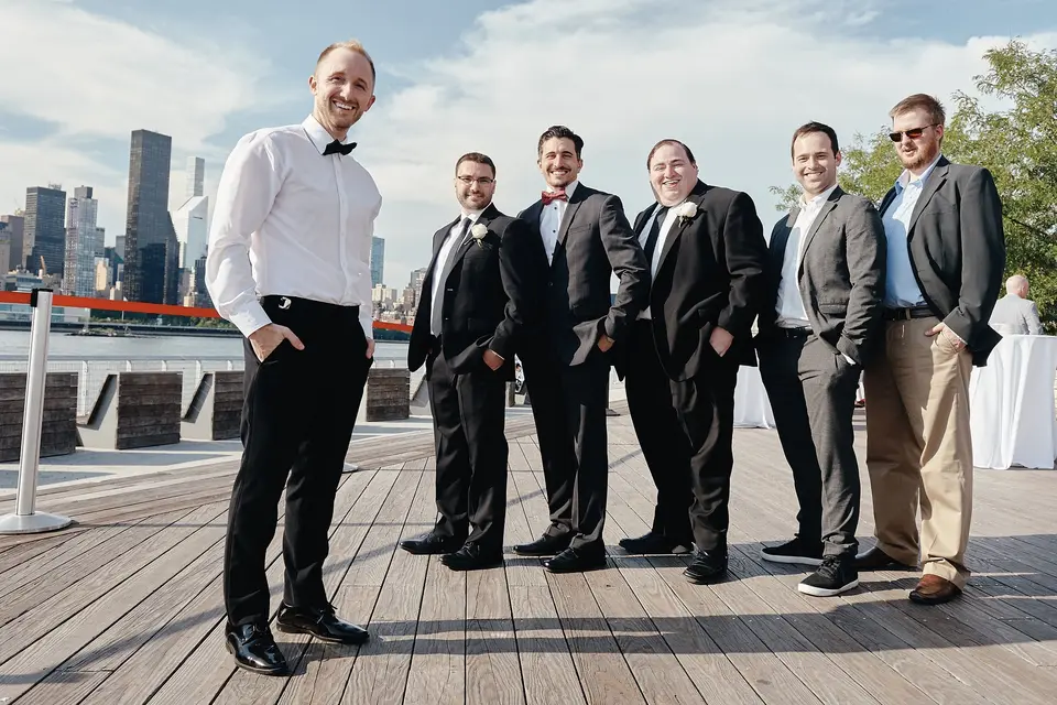 The groom and his groomsmen stand on the waterfront deck, the skyline behind them.