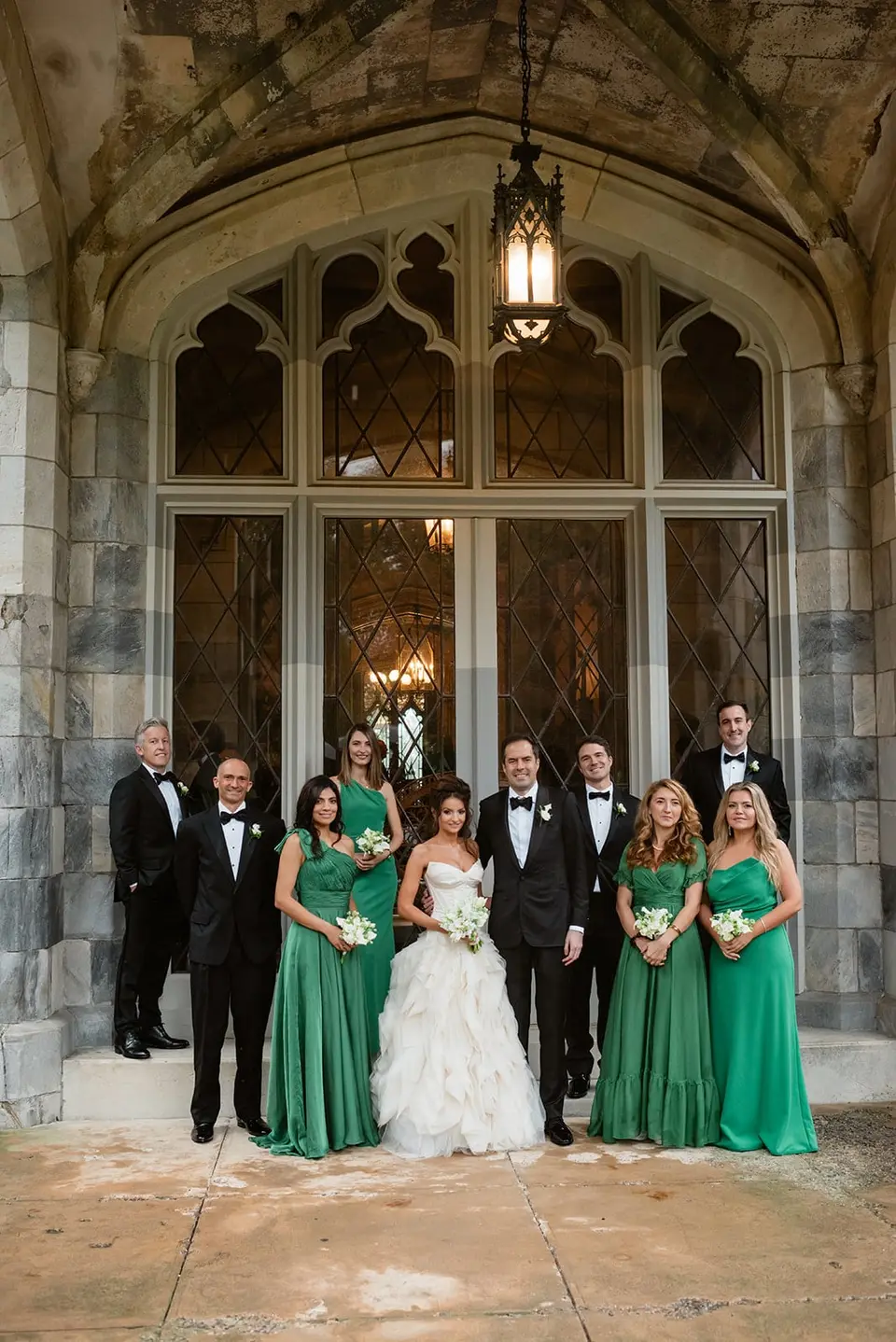 The wedding party beneath a Gothic arch at the mansion's entrance, the bridesmaids in emerald.