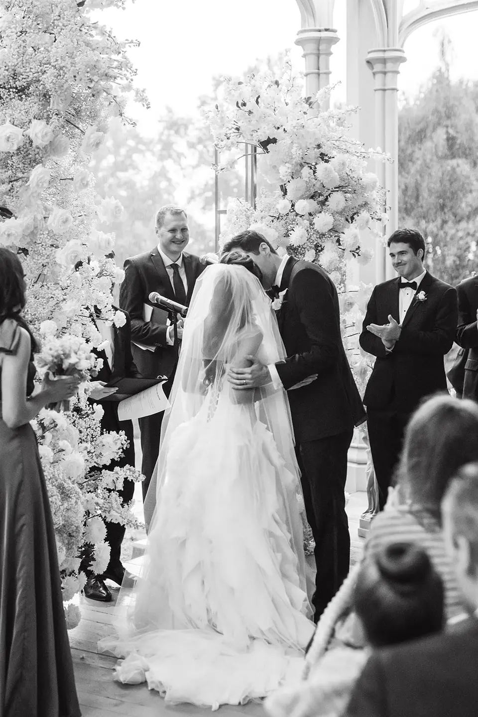 The first kiss at the altar, the groomsmen clapping. Black and white.