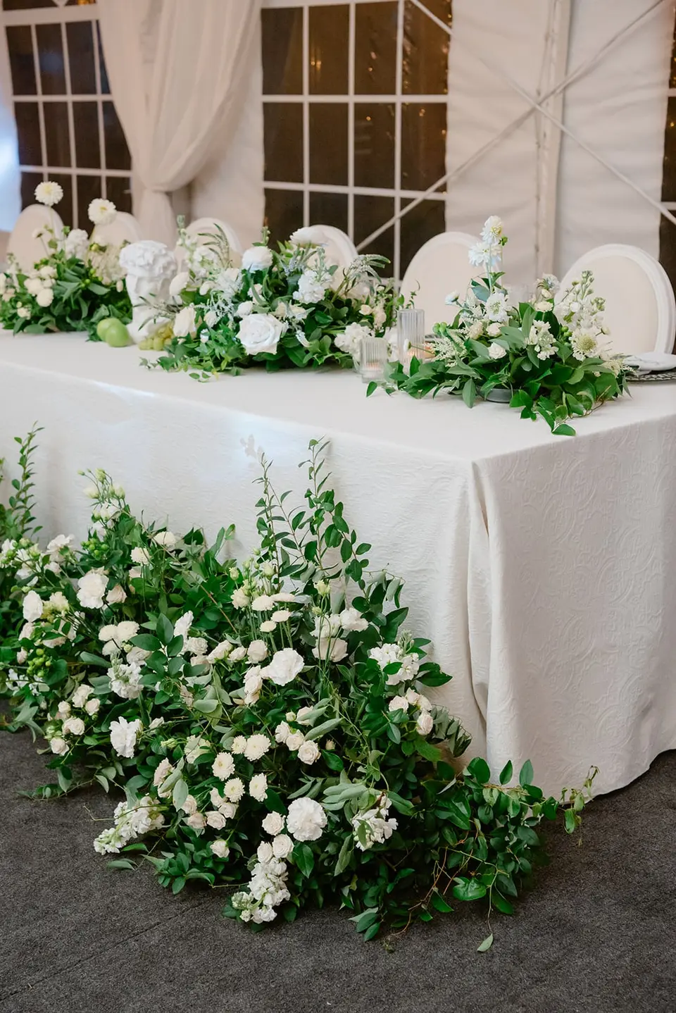 White flowers and greenery spilling from the head table to the floor.