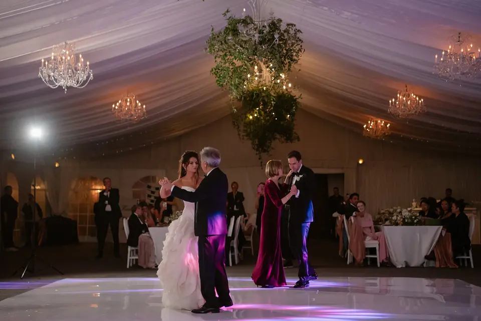 The bride dances with her father and the groom with his mother, beneath chandeliers and hanging greenery.