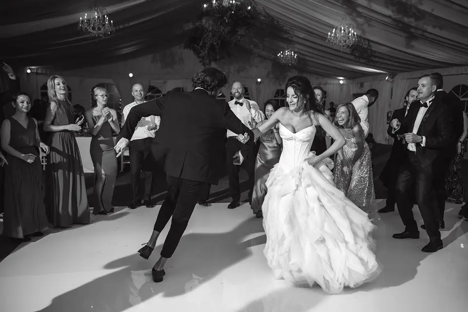 The bride and groom dance in a circle of clapping guests. Black and white.
