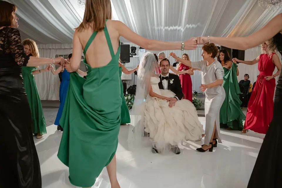 Guests join hands and dance in a circle around the seated bride and groom.