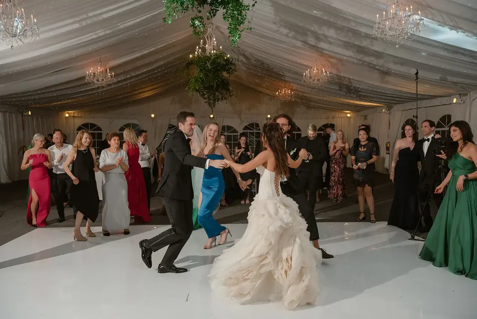 The bride and groom lead the dancing, guests in bright dresses around them.