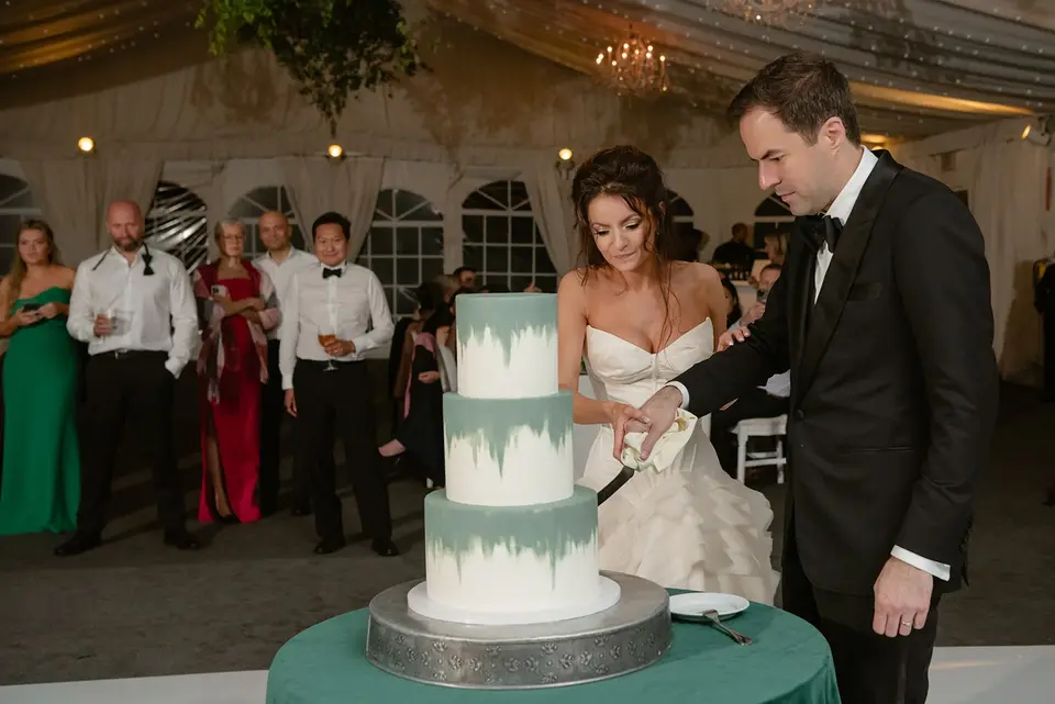 The bride and groom cut a three-tier cake brushed with green, guests watching.
