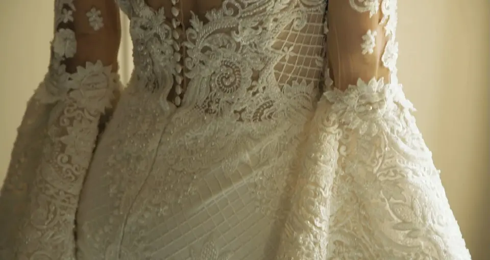 The morning of a wedding: the back of a lace gown, buttoned from the waist to the shoulders.