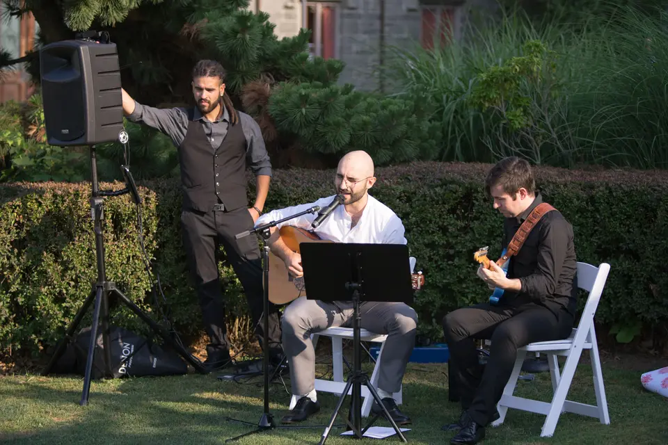 Three musicians play guitar and sing on the lawn.