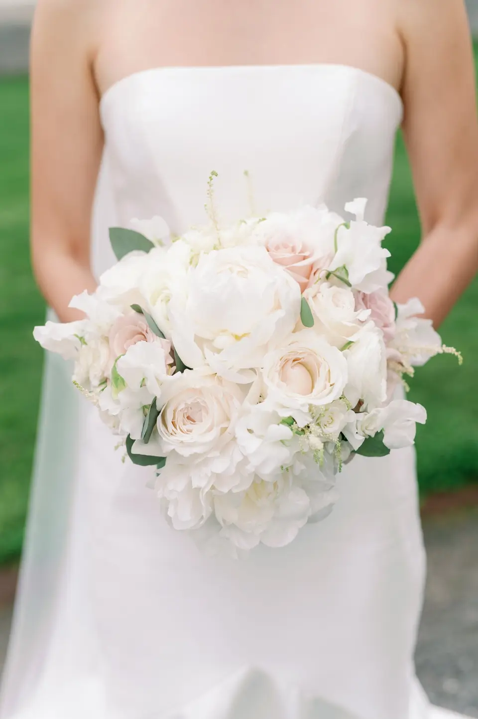 The bride holds a bouquet of white and blush roses against her strapless gown.