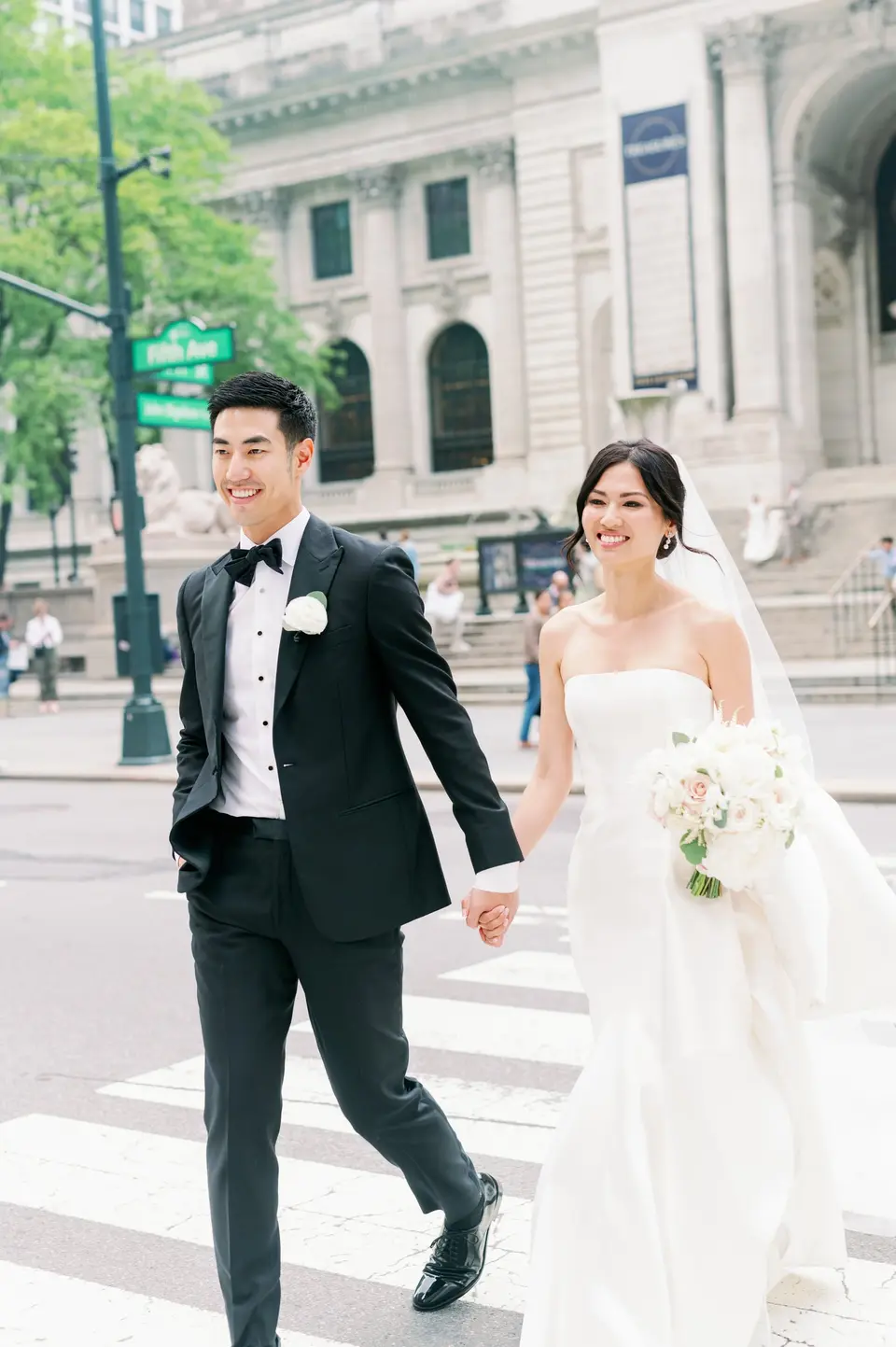 The bride and groom cross Fifth Avenue hand in hand in front of the Public Library.