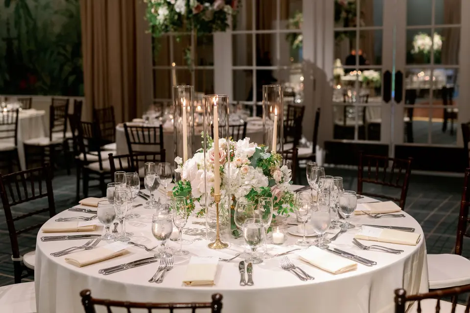 A round table set with tall taper candles and a low arrangement of blush flowers.