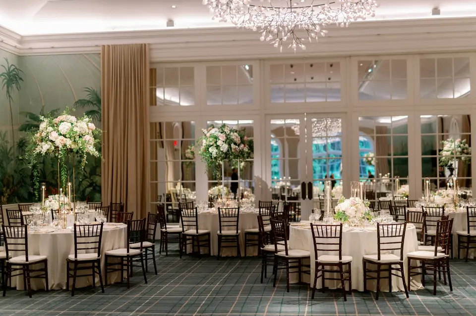 The dining room set for dinner, round tables with tall white arrangements beneath a crystal chandelier.