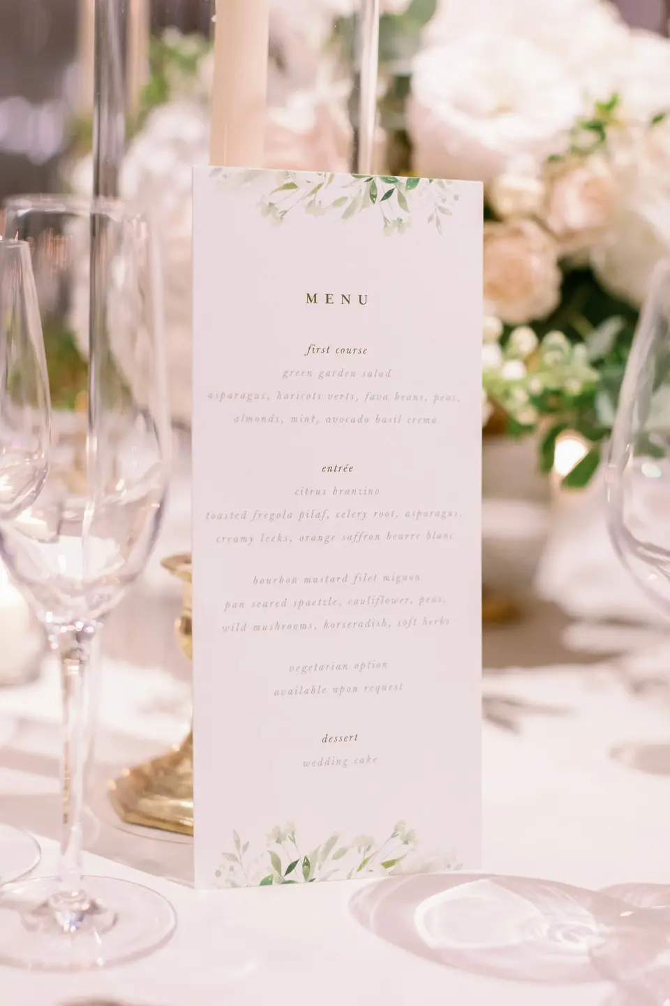 A menu card with watercolor leaves among glasses and white roses.