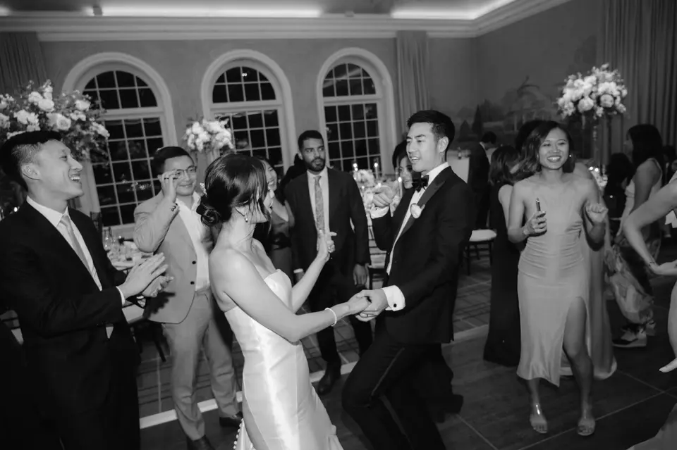 The bride and groom dance hand in hand among cheering friends. Black and white.