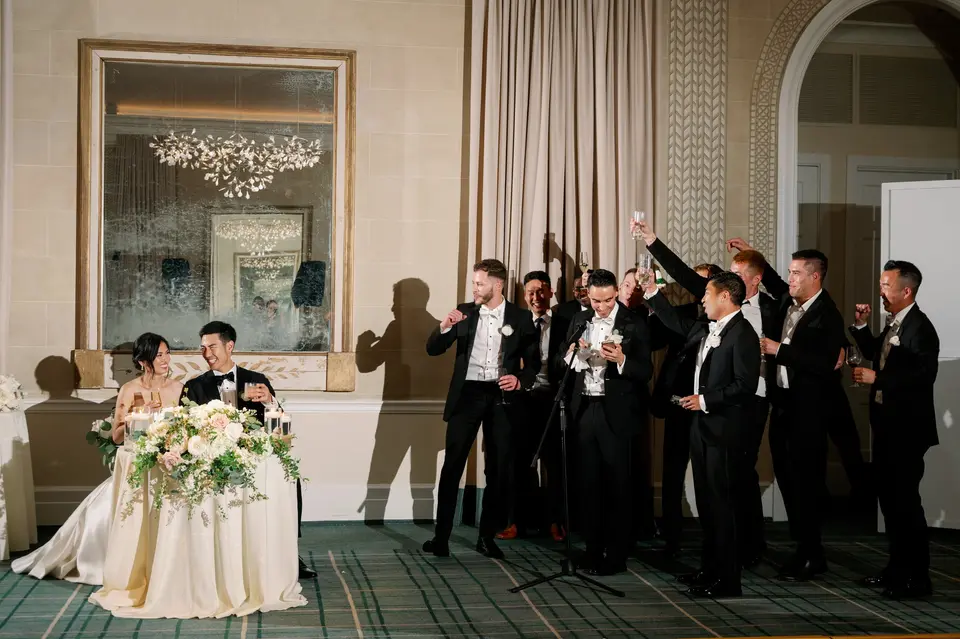The groomsmen raise their glasses in a toast as the couple watch from the sweetheart table.