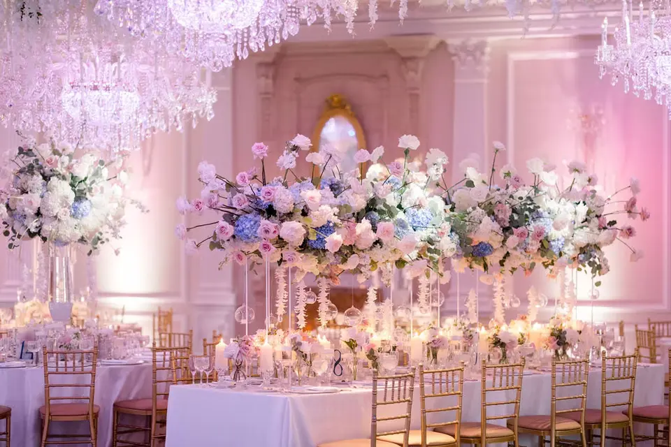 A reception room beneath hanging white flowers, long tables of white and blue arrangements under crystal chandeliers.