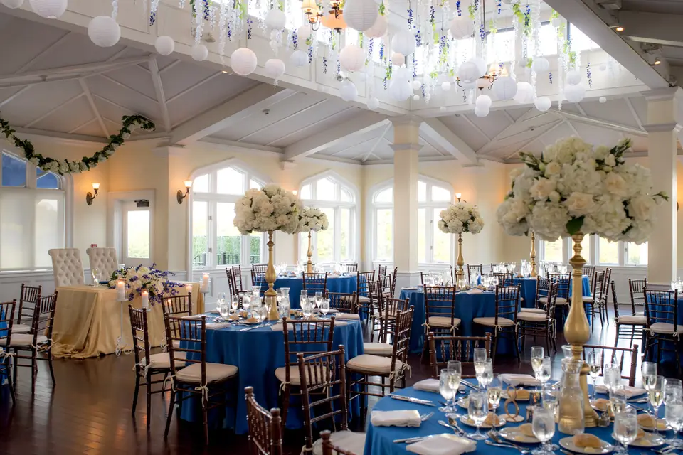 The reception room, round tables in deep blue linen with tall white arrangements beneath hanging paper lanterns.