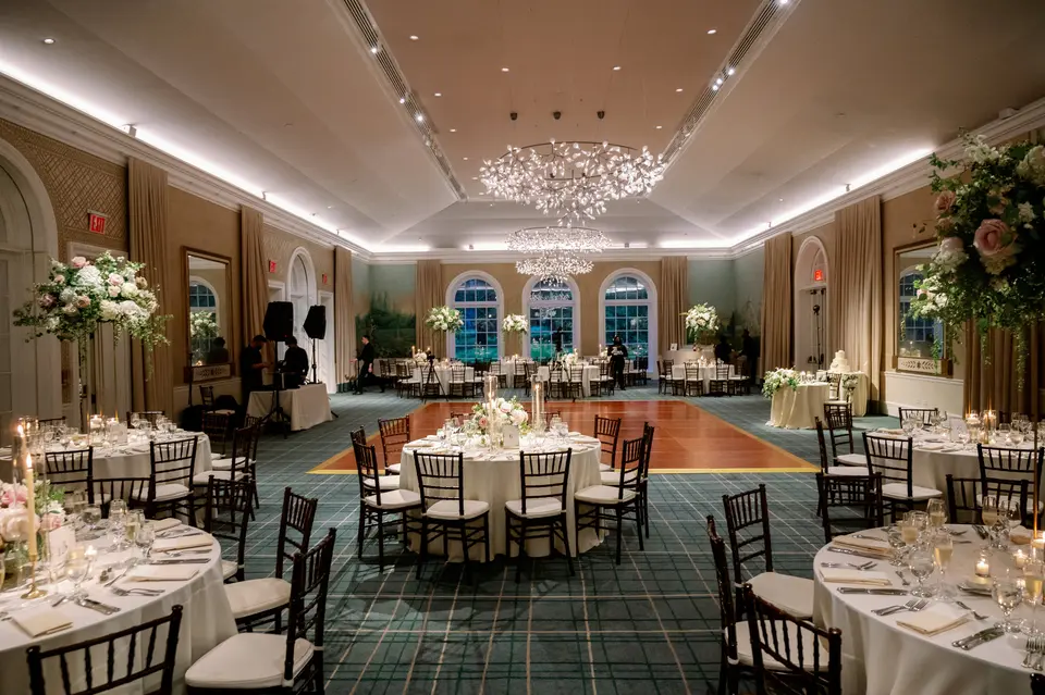 The reception room at the garden, round tables with candles and blush flowers beneath a sparkling chandelier.