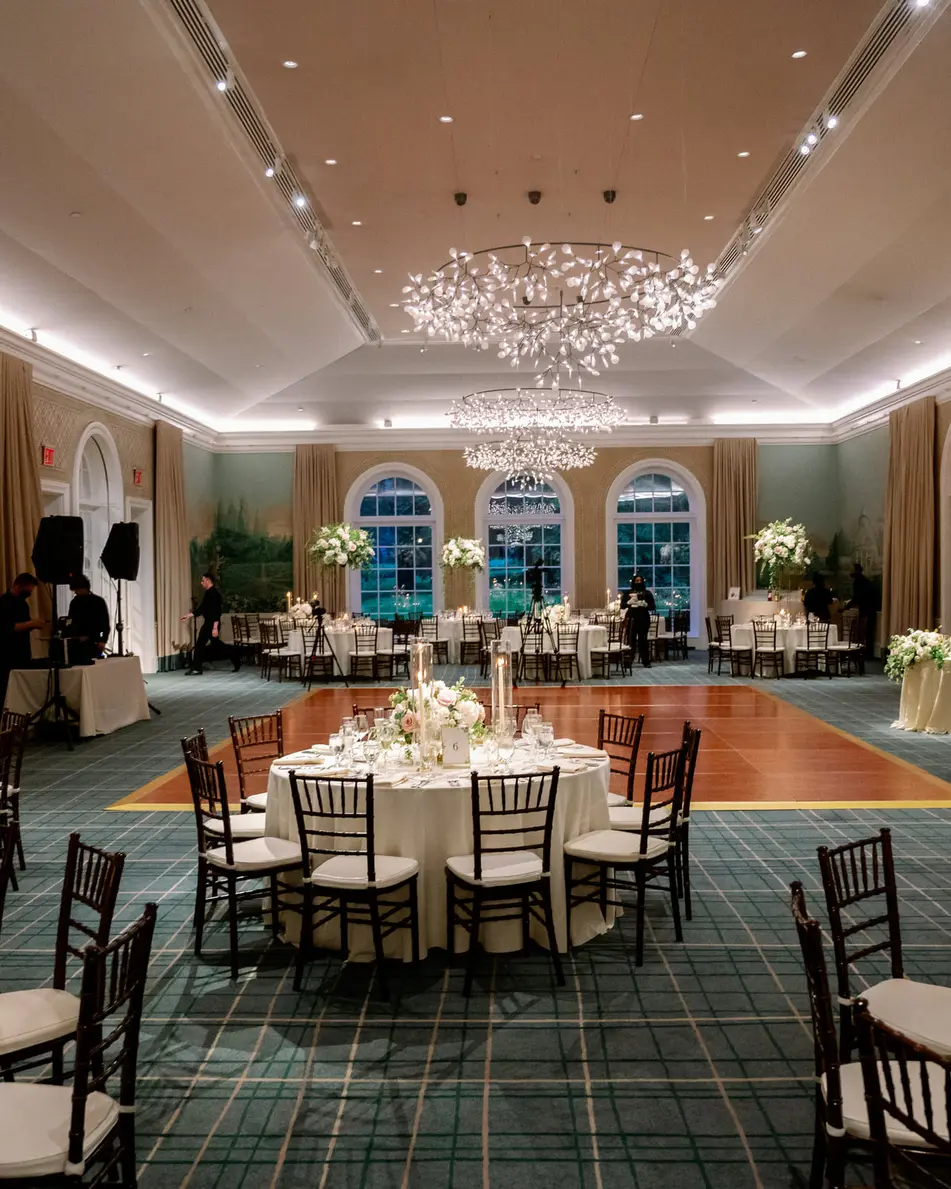 The reception room at the garden, round tables with candles and blush flowers beneath a sparkling chandelier.
