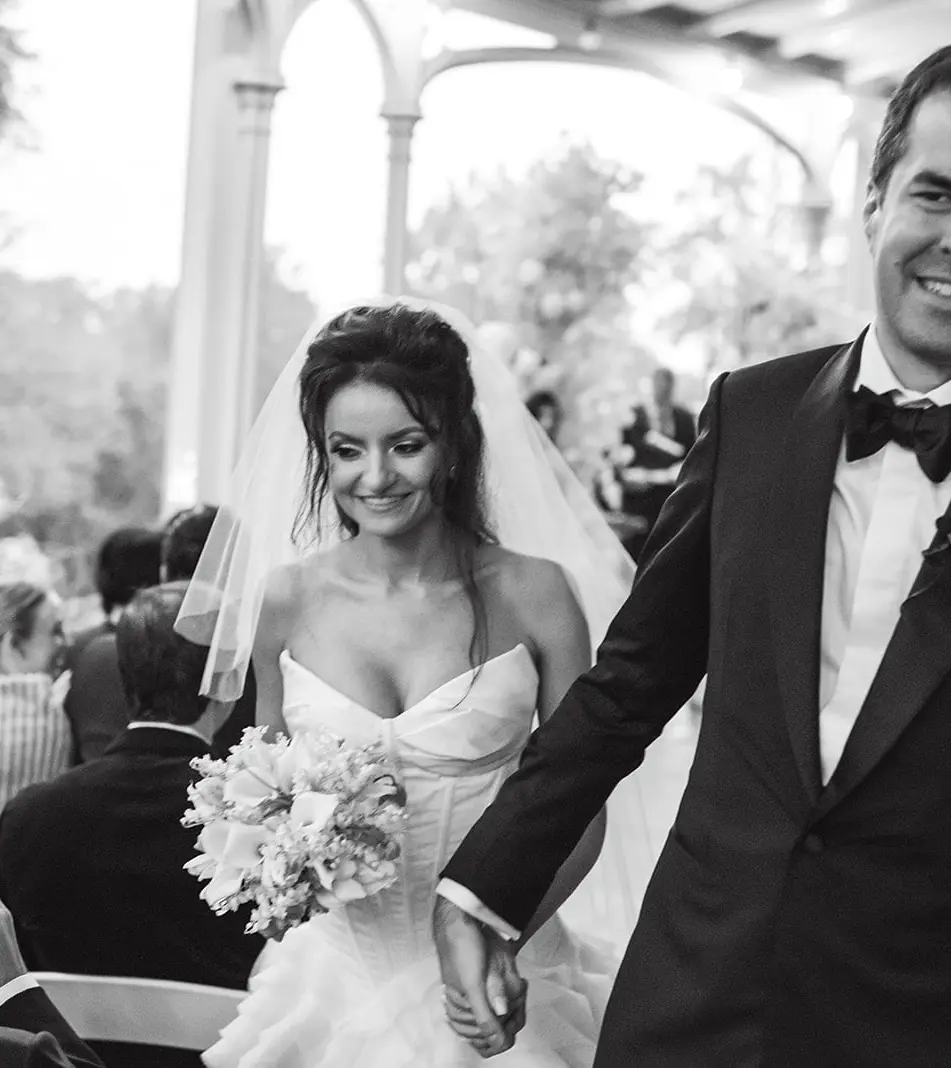 The couple walk back up the aisle hand in hand, smiling. Black and white.