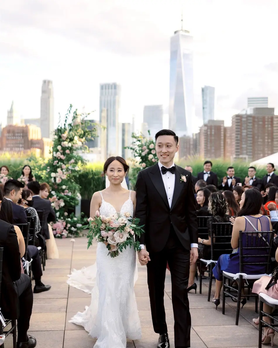 Married, the couple walk back up the aisle hand in hand, guests standing on either side, the towers of Lower Manhattan behind.