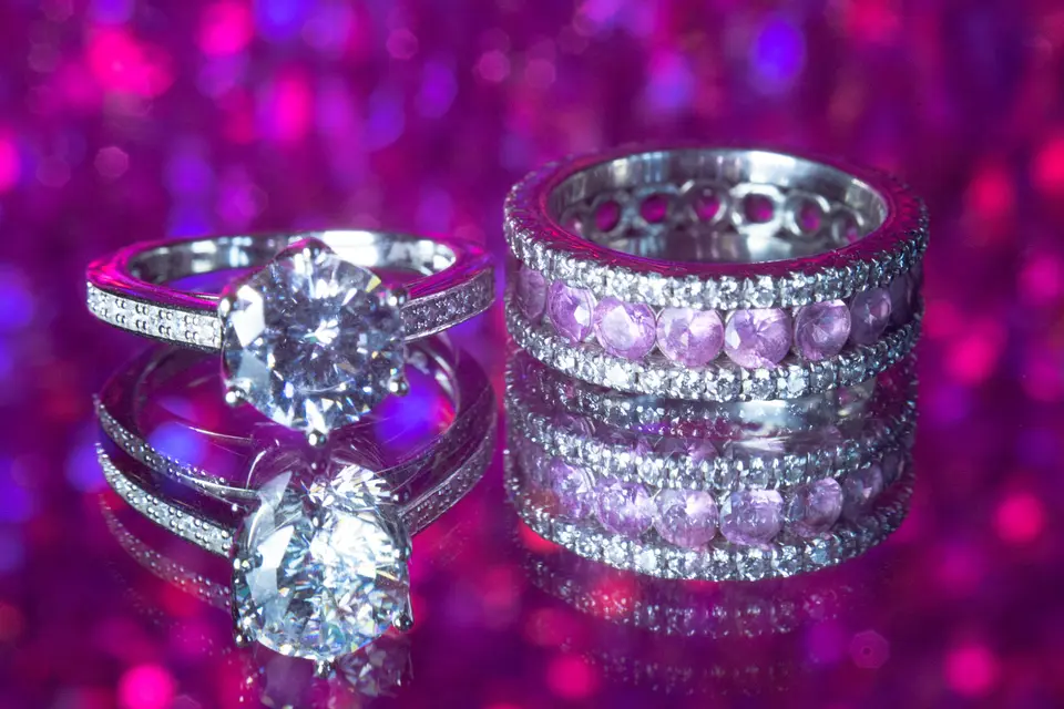 The engagement ring and wedding bands in pink and violet light.