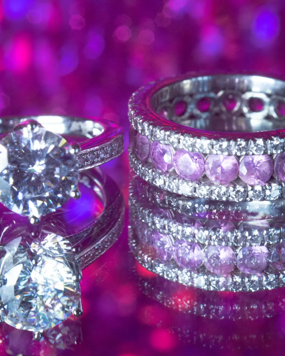 The engagement ring and wedding bands in pink and violet light.