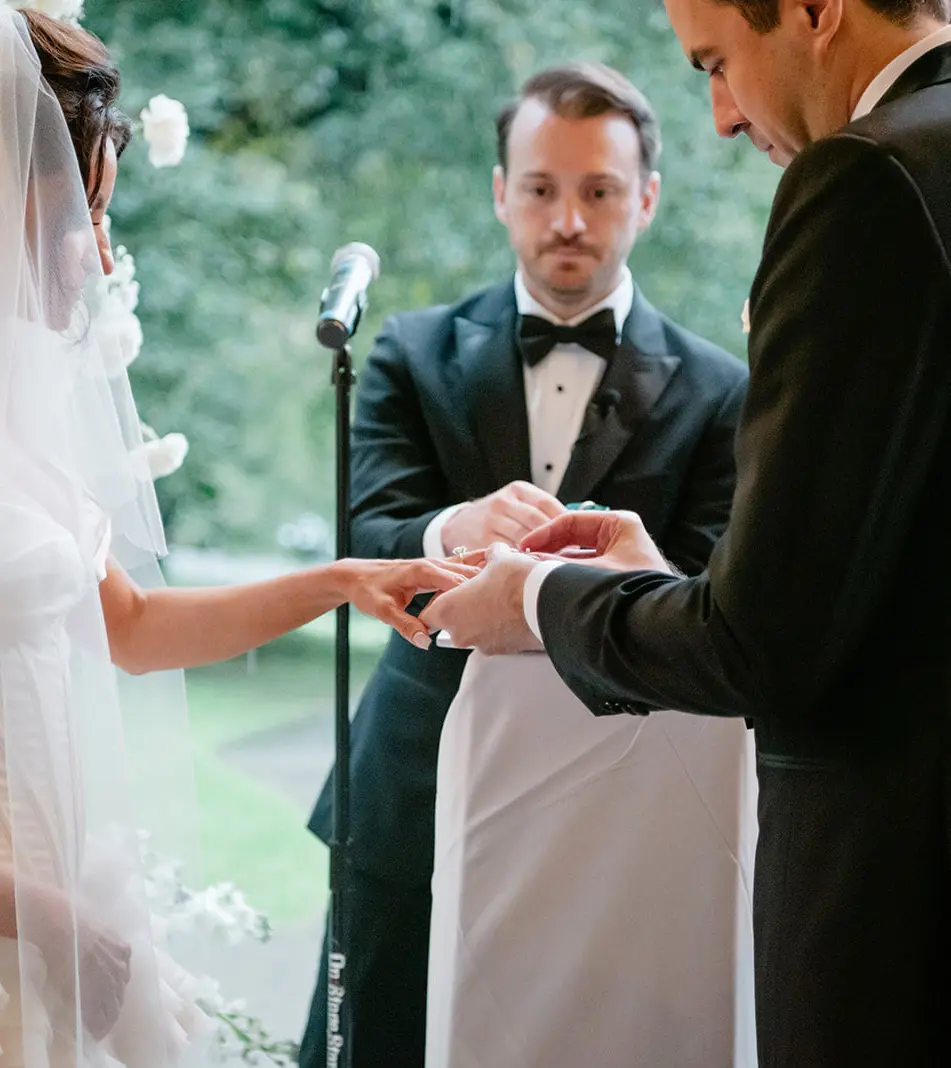 The groom slips the ring onto the bride's finger among the white flowers.