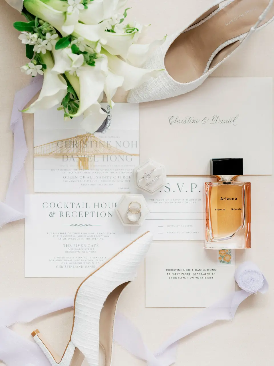 The invitation suite laid out with white calla lilies, ivory heels, a ring box and a bottle of perfume.
