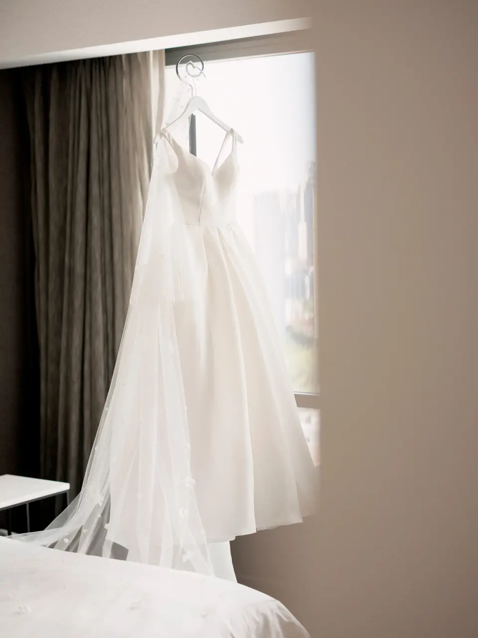 The wedding gown hanging in a sunlit hotel window.