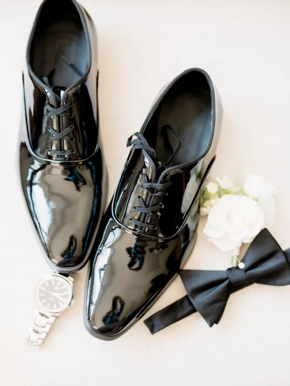 The groom's patent leather shoes with a black bow tie, a watch and a white boutonniere.