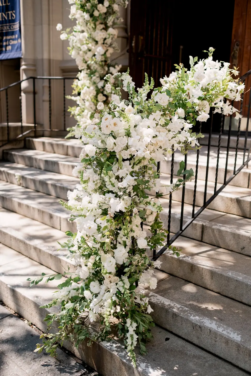 A cascade of white flowers and greenery along the railing of the church steps.