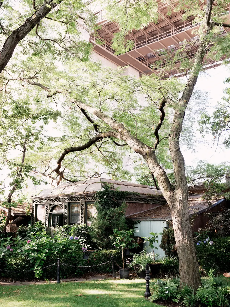 The garden at The River Café beneath the Brooklyn Bridge, leafy trees overhead.