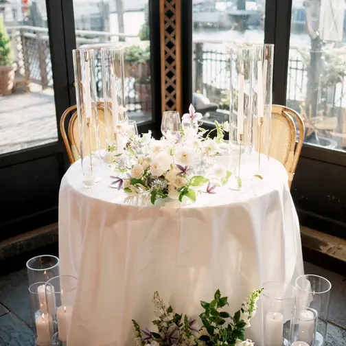 A round sweetheart table dressed in white linen and candles, set in a window overlooking the East River at The River Café.