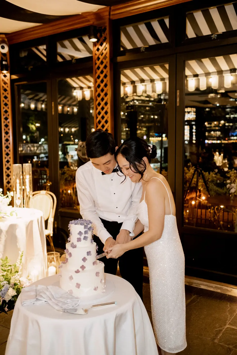 The bride and groom cut a white cake decorated with lavender flowers.