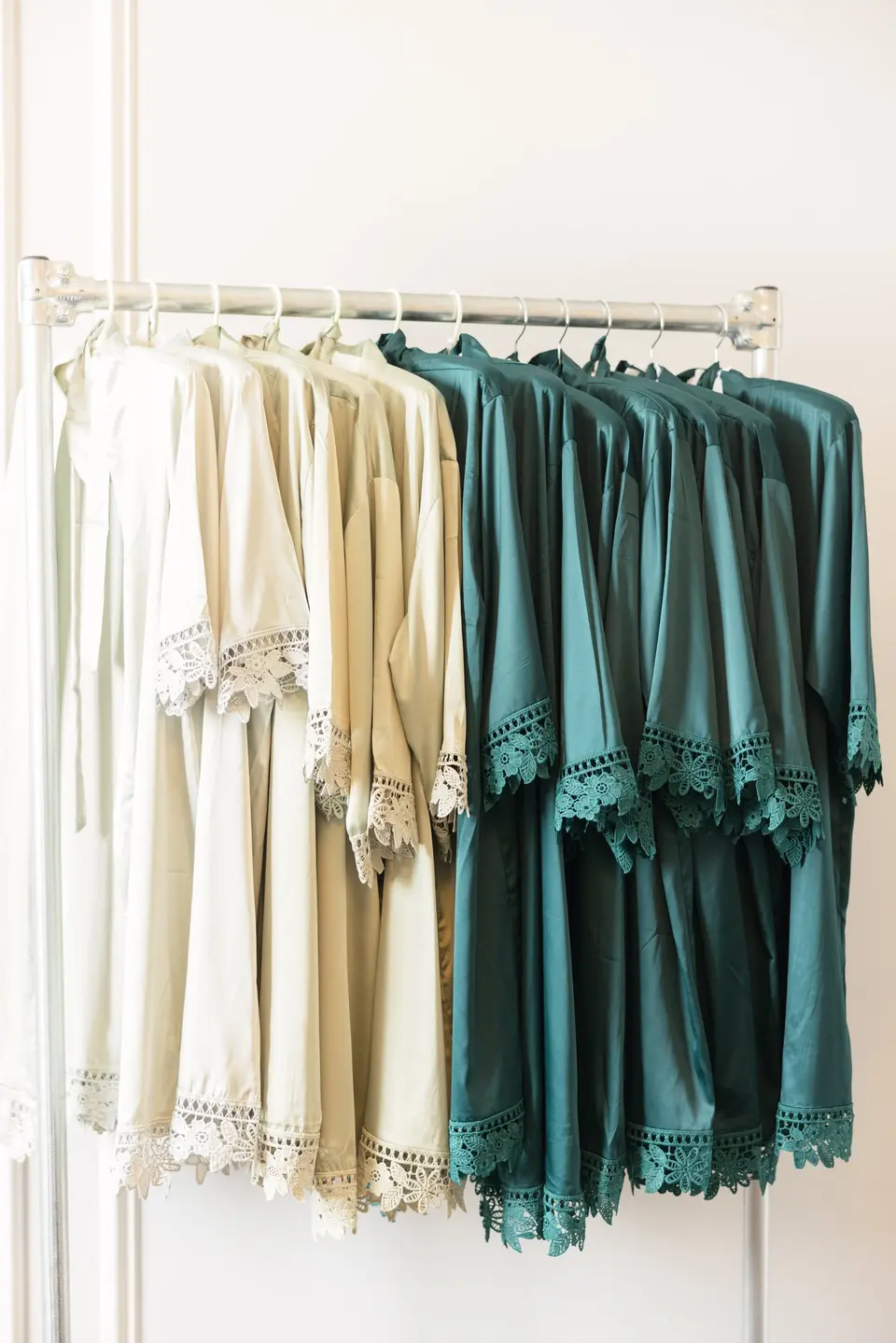 Lace-trimmed robes in ivory, gold and emerald on a rail, ready for the bride and bridesmaids.