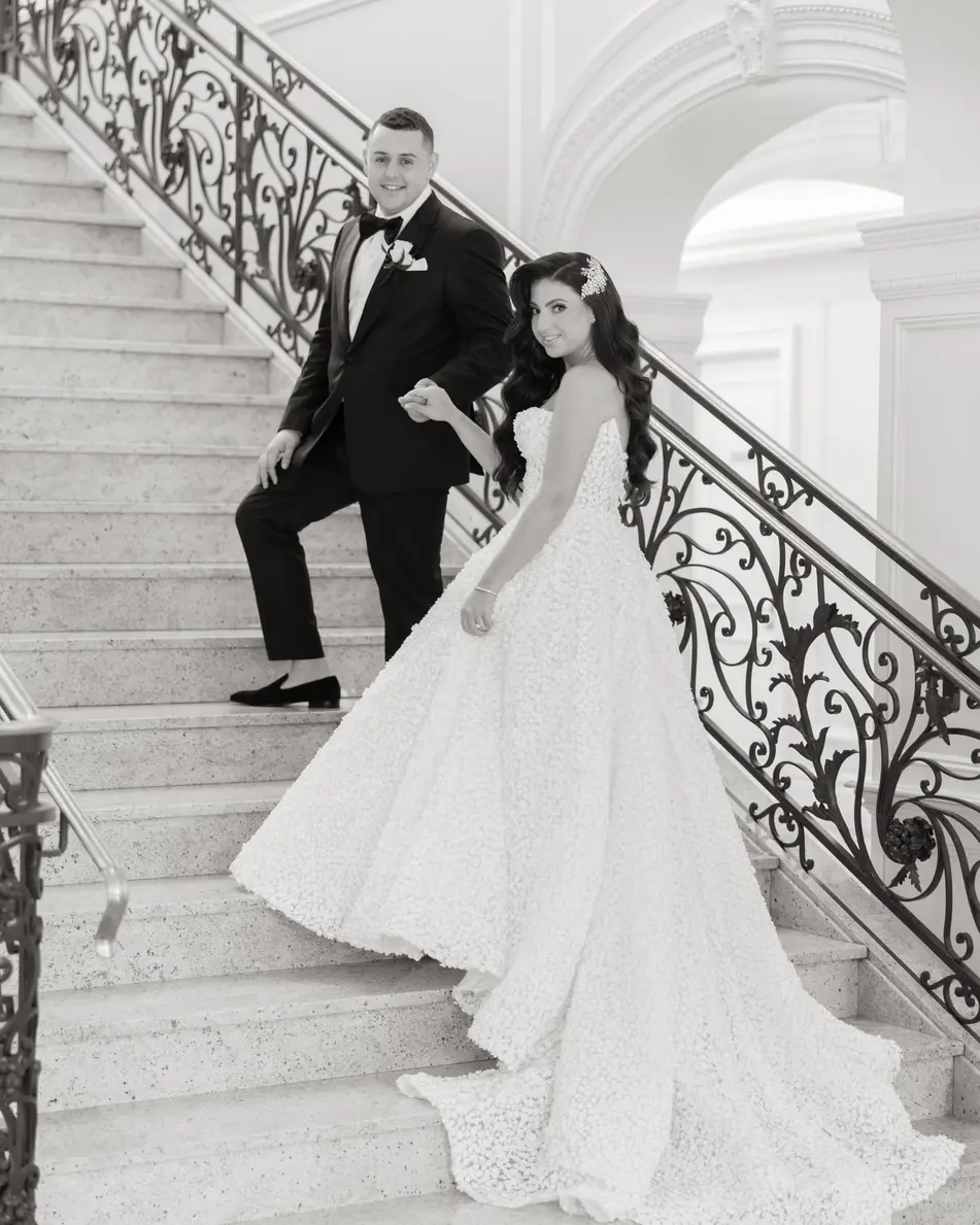 The bride and groom on the marble staircase, her train spread down the steps. Black and white.