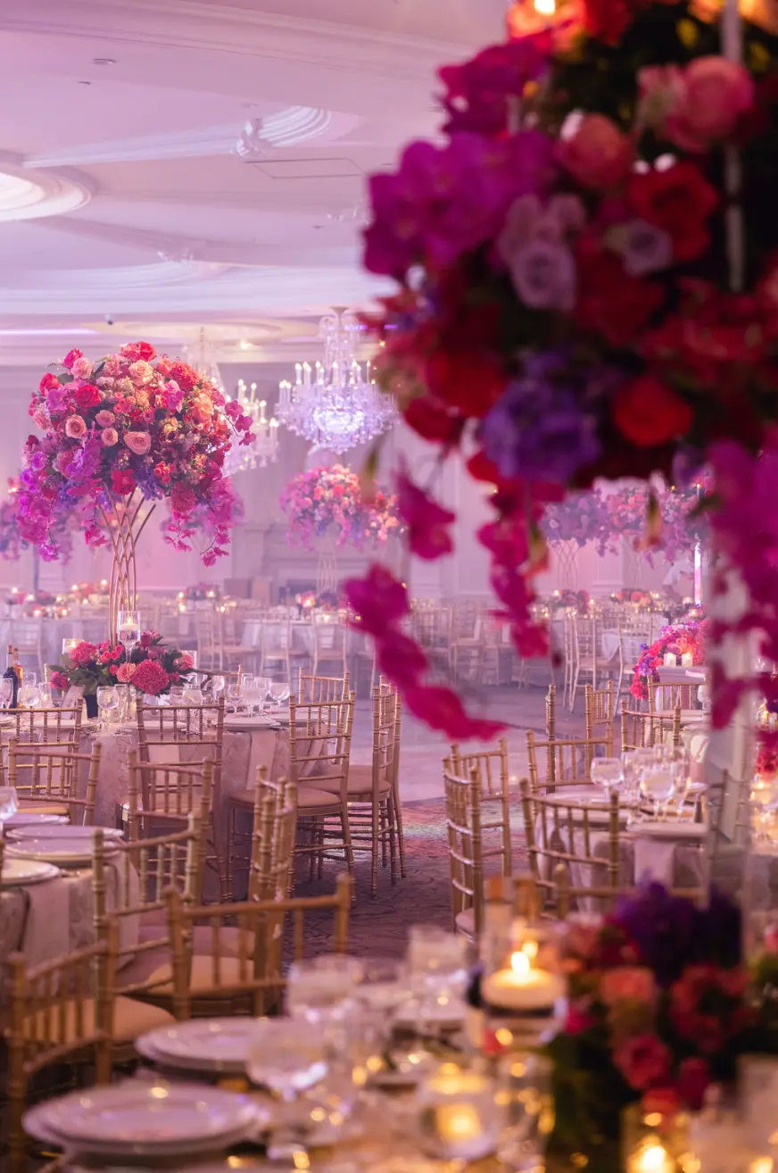 Tall arrangements of red, pink and purple flowers above gold chairs in the ballroom.