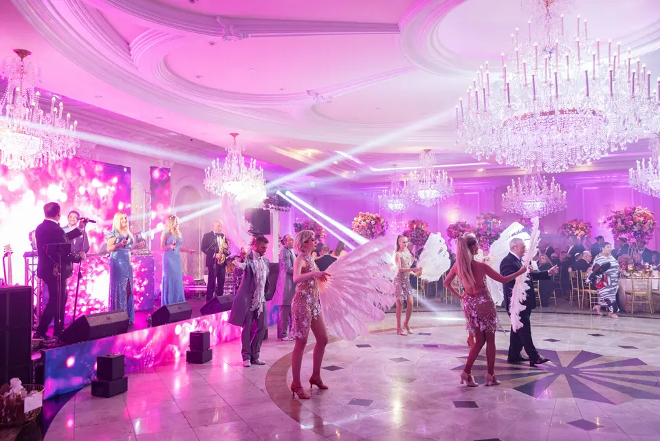 Dancers in feathered costumes and a band on stage fill the dance floor with light.