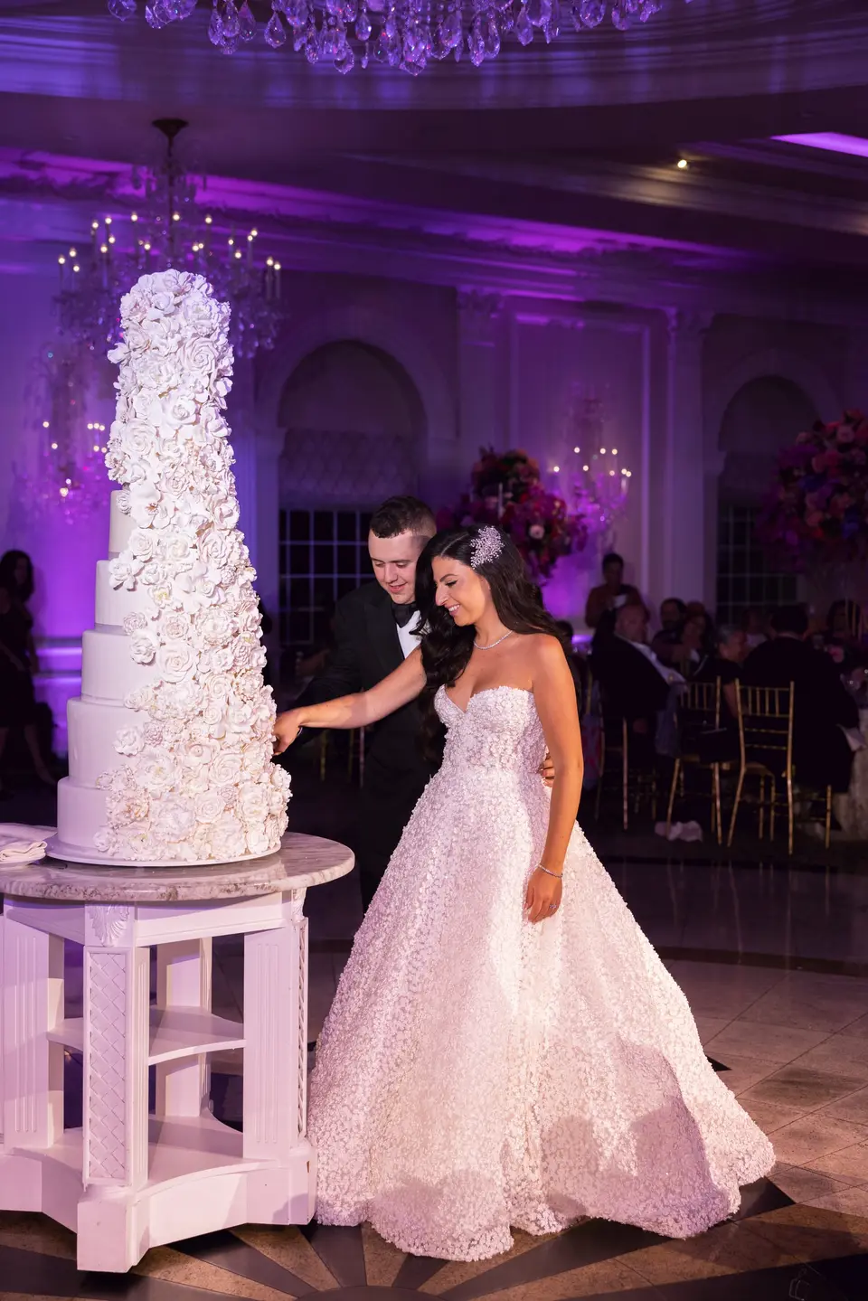 The bride and groom cut a towering white cake covered in sugar flowers.