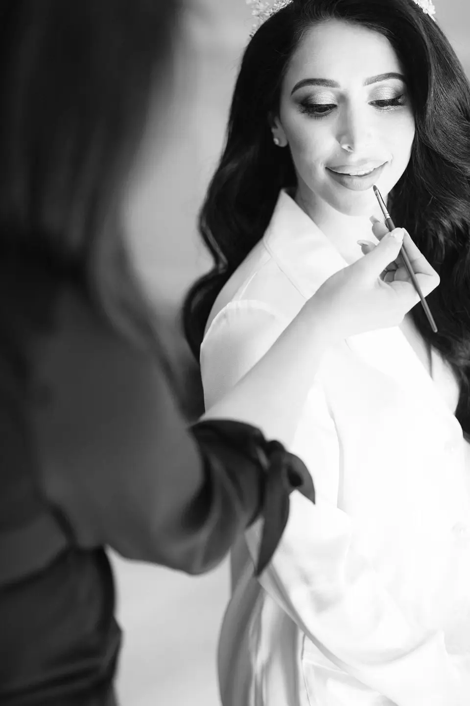 The bride's lipstick is brushed on as she gets ready, a tiara in her hair. Black and white.