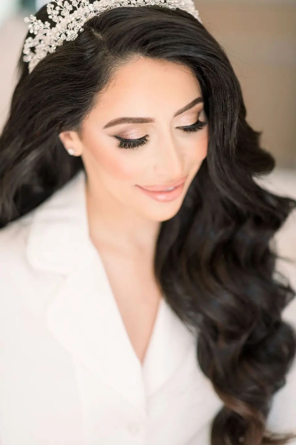 The bride in a white robe and a crystal tiara, her long hair in waves.
