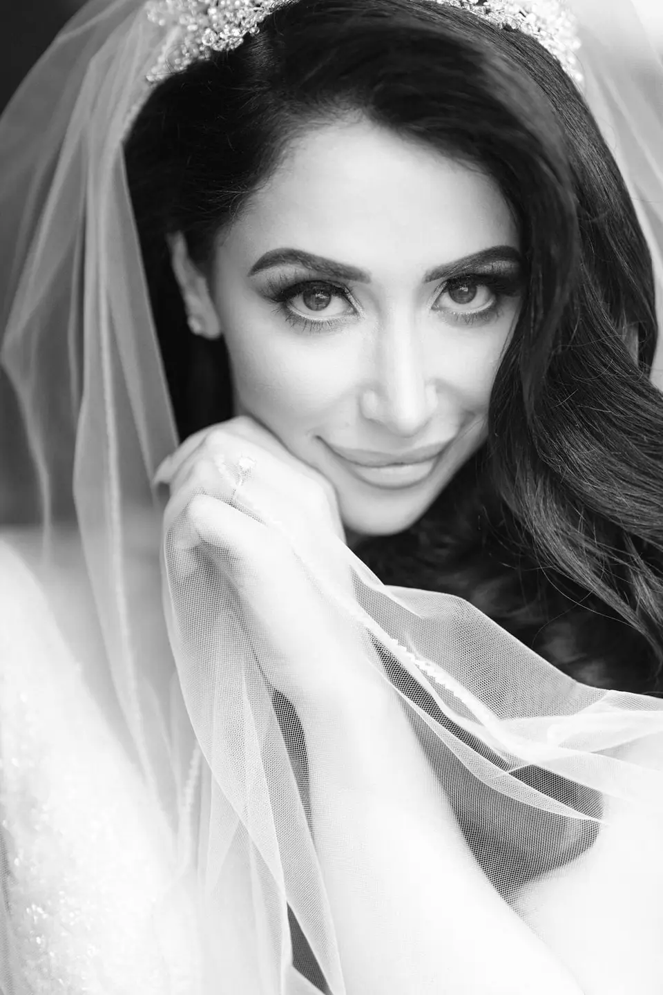 The bride rests her chin on her hand beneath her veil. Black and white.