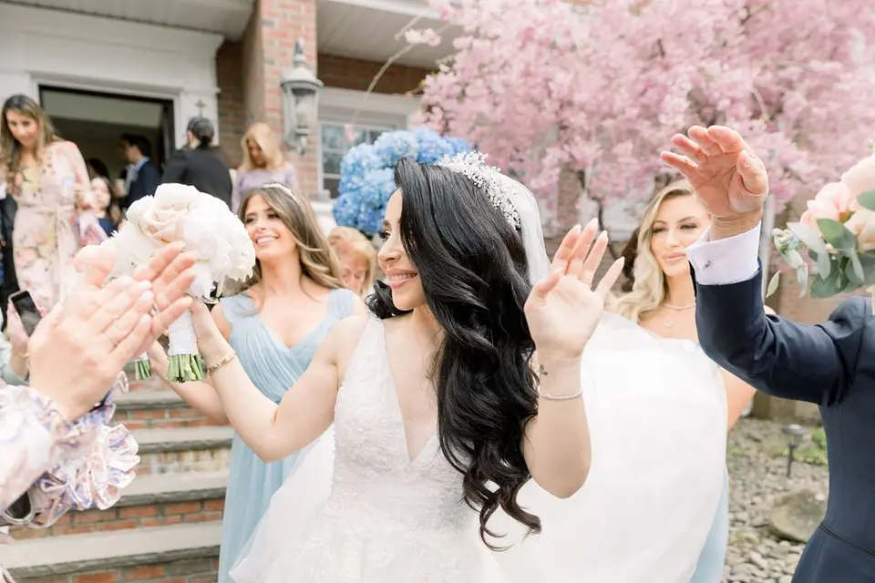 The bride dances with her bridesmaids outside the house, hands raised.