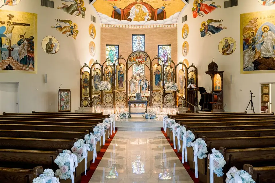 The church interior, walls of painted icons above the altar and blue and white flowers along the pews.