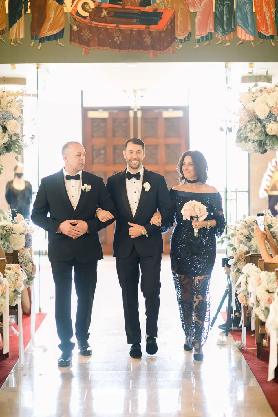 The groom walks down the aisle between his parents.