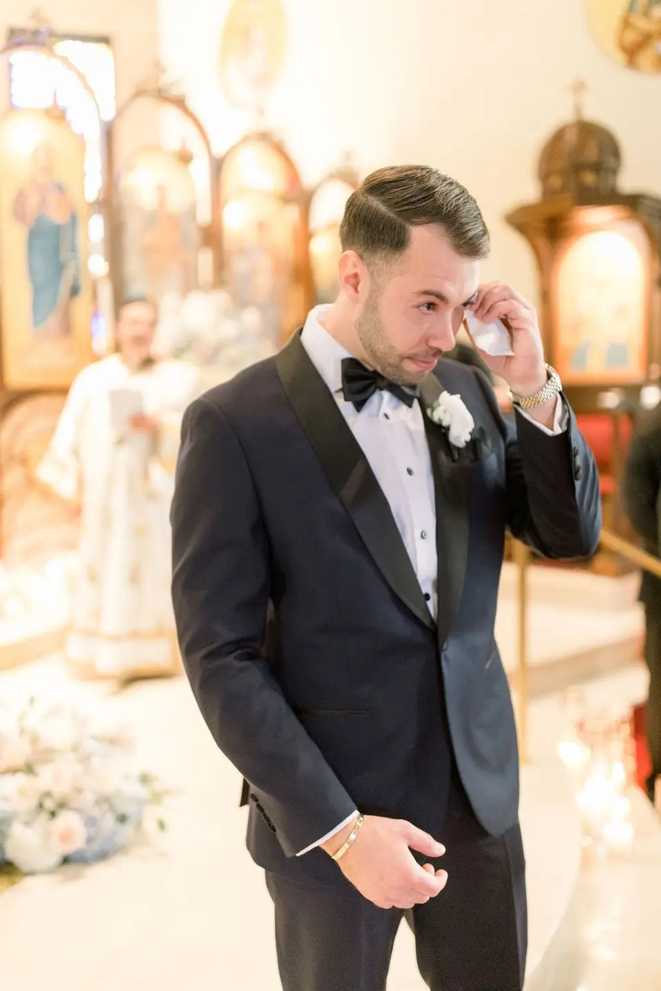 The groom wipes away a tear as he waits at the altar.