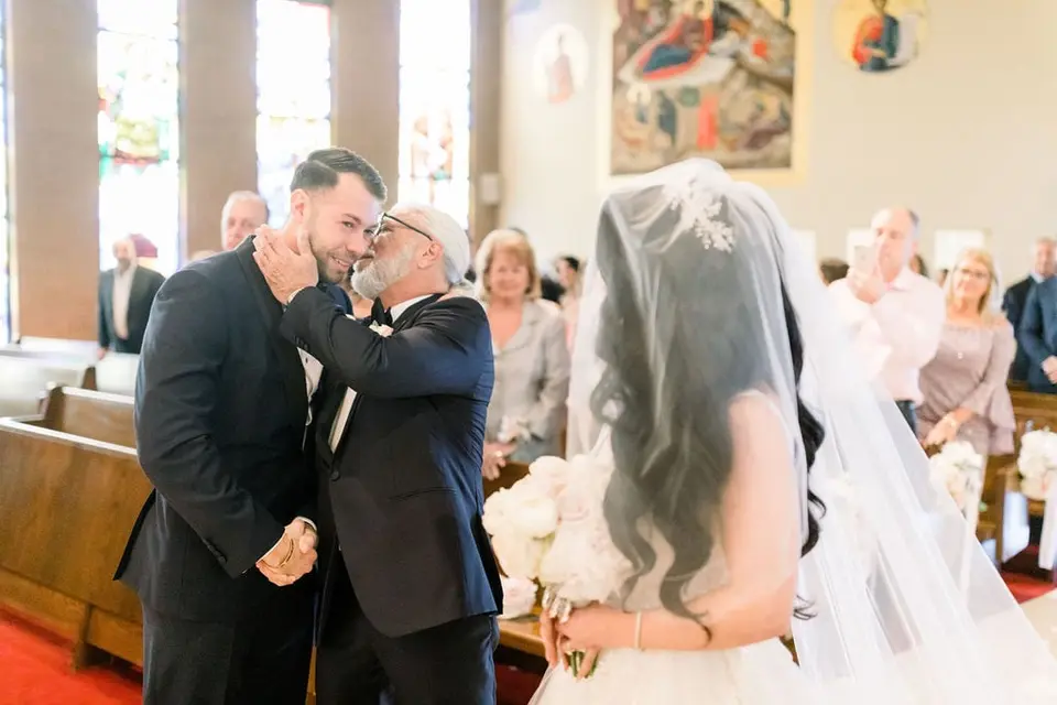 At the altar, the bride's father embraces the groom as he gives her away.